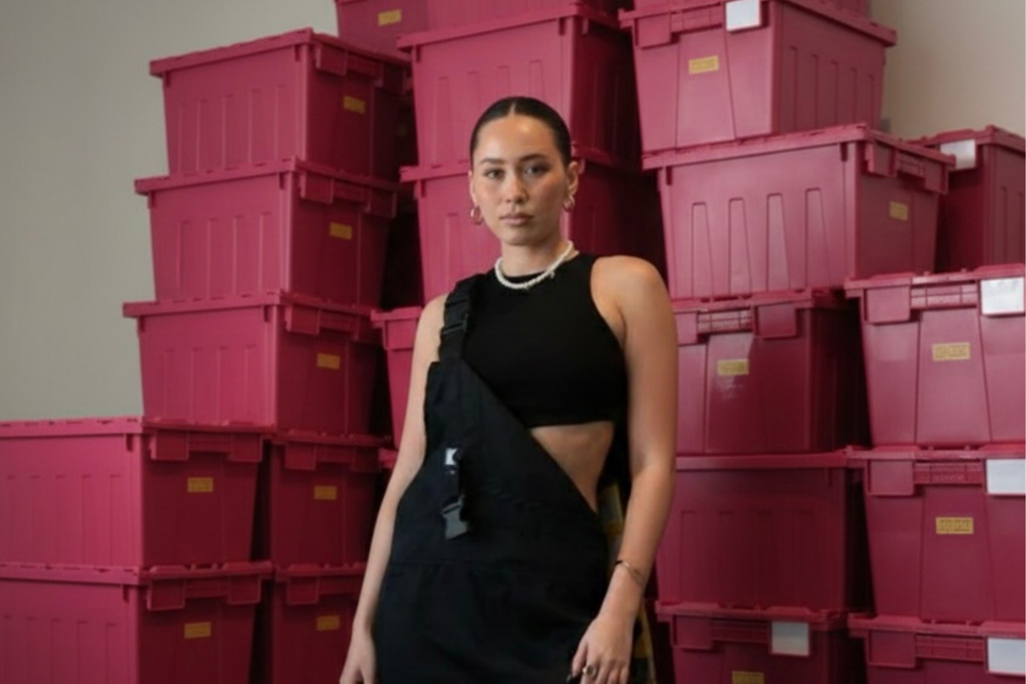Person in black outfit standing in front of stacked pink storage boxes